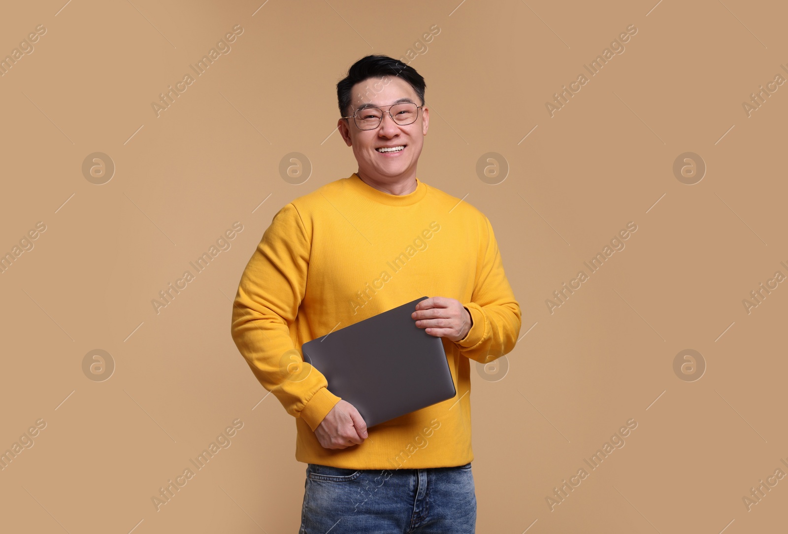 Photo of Happy man with laptop on beige background, space for text