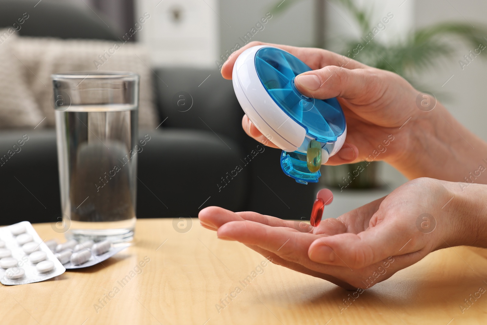 Photo of Woman with pills, organizer and glass of water at light wooden table, closeup