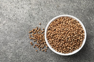 Dried coriander seeds in bowl on gray textured table, top view. Space for text