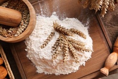 Photo of Pile of wheat flour and spikes on wooden table, flat lay