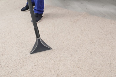 Man removing dirt from carpet with vacuum cleaner indoors, closeup. Space for text