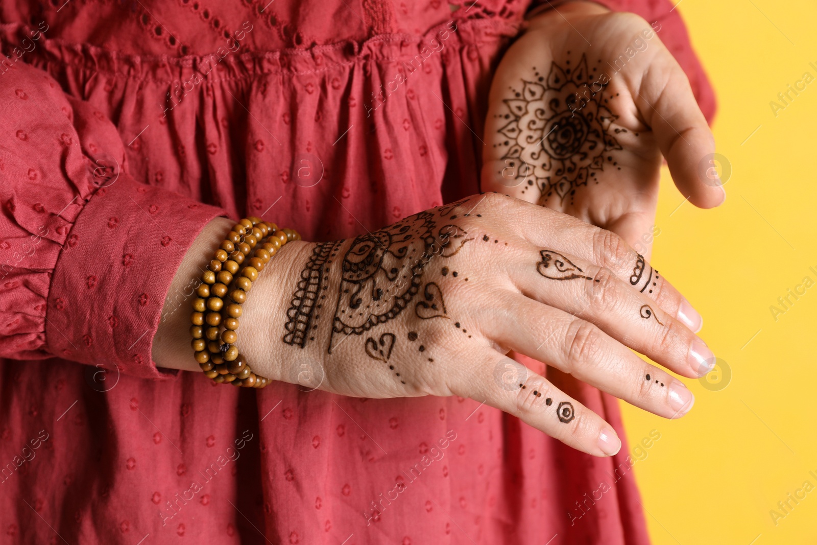 Photo of Woman with beautiful henna tattoos on hands against yellow background, closeup. Traditional mehndi