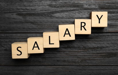 Word Salary made with cubes on dark wooden table, flat lay