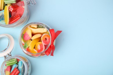 Tasty colorful jelly candies in glass jars on light blue background, flat lay. Space for text