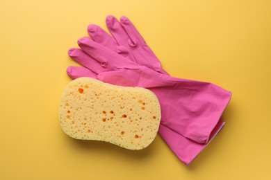 Photo of Sponge and gloves on yellow background, top view
