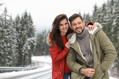 Photo of Couple in warm clothes near snowy forest, space for text. Winter vacation