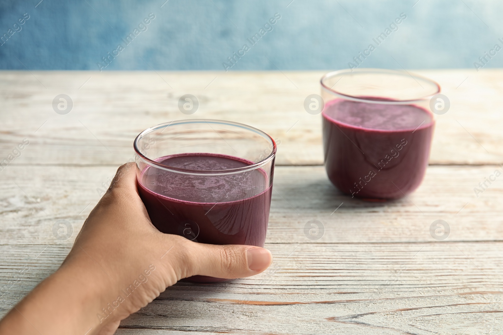 Photo of Woman holding glass of delicious acai juice on table, closeup