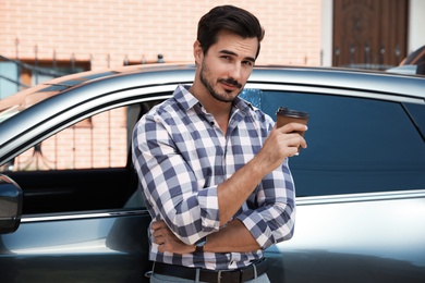 Attractive young man with cup of coffee near luxury car outdoors