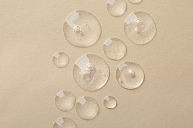 Photo of Drops of cosmetic serum on beige background, top view