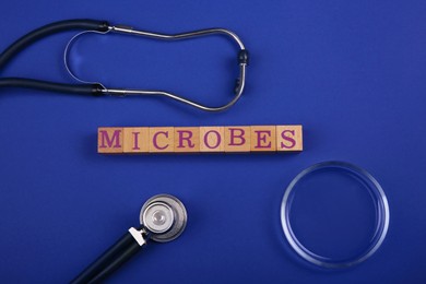 Photo of Word Microbes made with wooden cubes, stethoscope and magnifying glass on blue background, top view