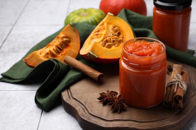 Jar of delicious pumpkin jam and ingredients on tiled surface