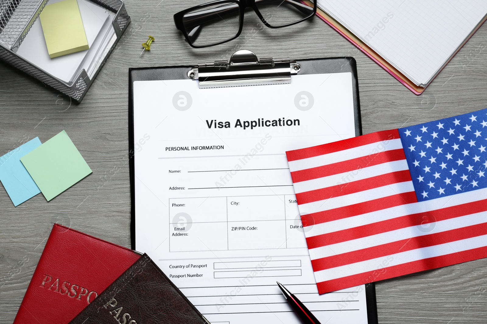 Photo of Visa application form, American flag, passports and stationery on wooden table, flat lay