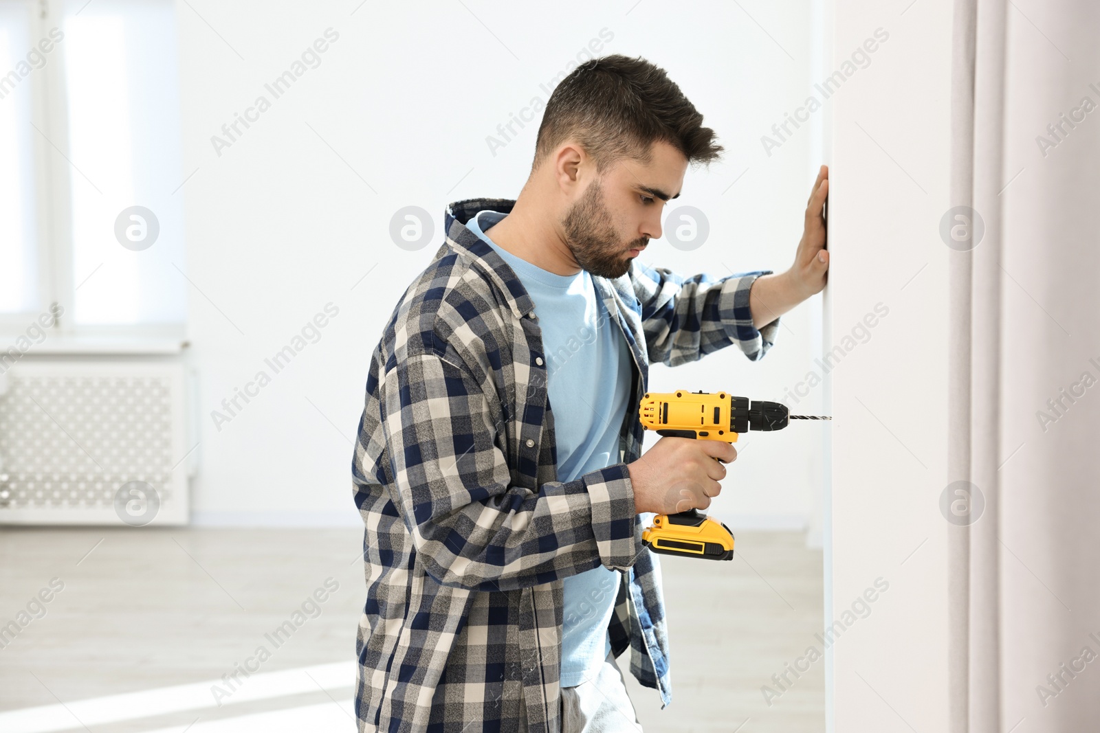 Photo of Young handyman working with electric drill at home