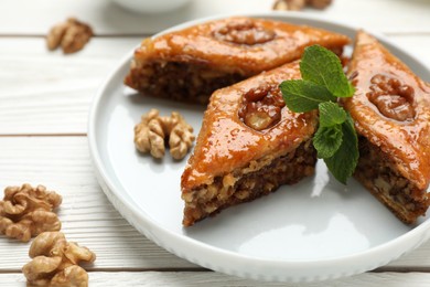 Photo of Delicious sweet baklava with walnuts and mint on white wooden table, closeup