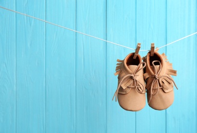 Baby shoes on laundry line against color wooden background, space for text. Child accessories