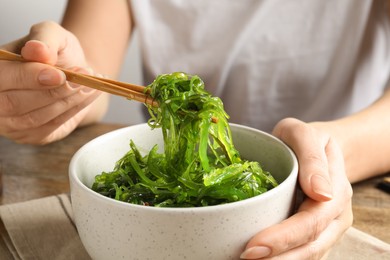 Photo of Woman eating Japanese seaweed salad at table, closeup