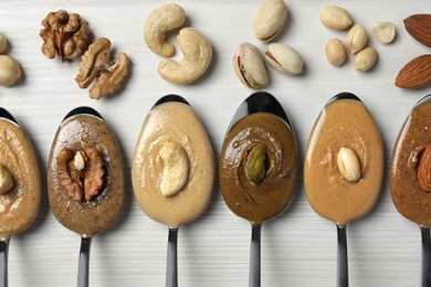 Tasty nut butters in spoons and raw nuts on white wooden table, flat lay