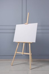 Wooden easel with blank canvas near grey wall indoors. Space for text