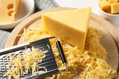 Grated, whole pieces of cheese and grater on table, closeup