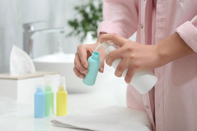 Photo of Woman pouring cosmetic product into plastic bottle over white countertop in bathroom, closeup and space for text. Bath accessories