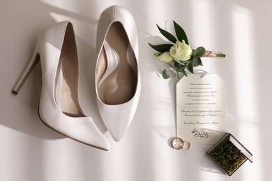 Photo of Beautiful bride's shoes, wedding rings, glass box, boutonniere and invitation on white background, top view