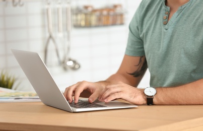 Photo of Young man working with laptop at table in kitchen, closeup