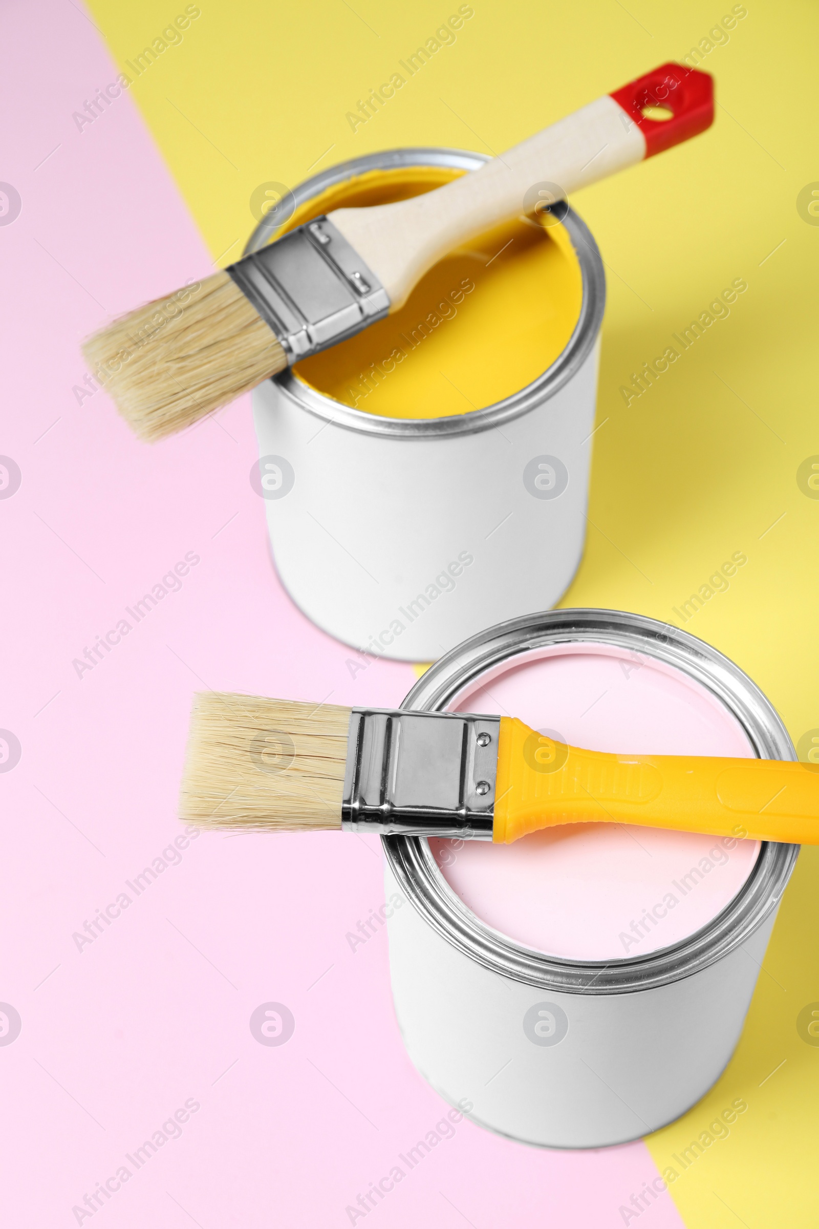 Photo of Cans of colorful paints with brushes on color background