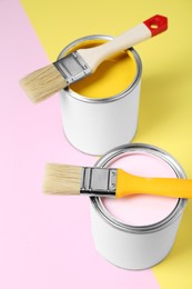 Photo of Cans of colorful paints with brushes on color background