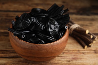 Photo of Tasty black candies and dried sticks of liquorice root on wooden table, closeup