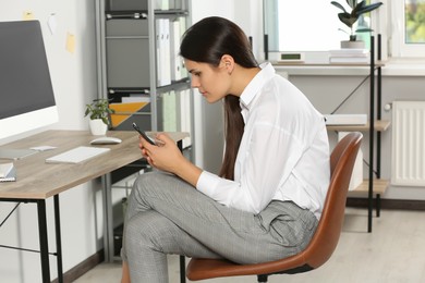 Young woman with bad posture using smartphone while sitting in office. Symptom of scoliosis