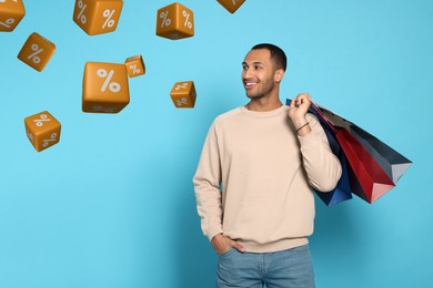 Image of Discount offer. Happy man with paper shopping bags looking at falling cubes with percent signs on light blue background