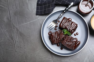 Photo of Delicious chocolate brownies with sweet syrup and mint served on grey table, flat lay. Space for text