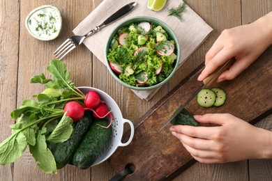 Photo of Woman cooking salad with radish and cucumber at wooden table, top view