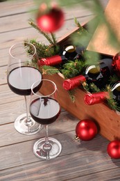 Wooden crate with bottles of wine, glasses, fir twigs and red Christmas balls on table