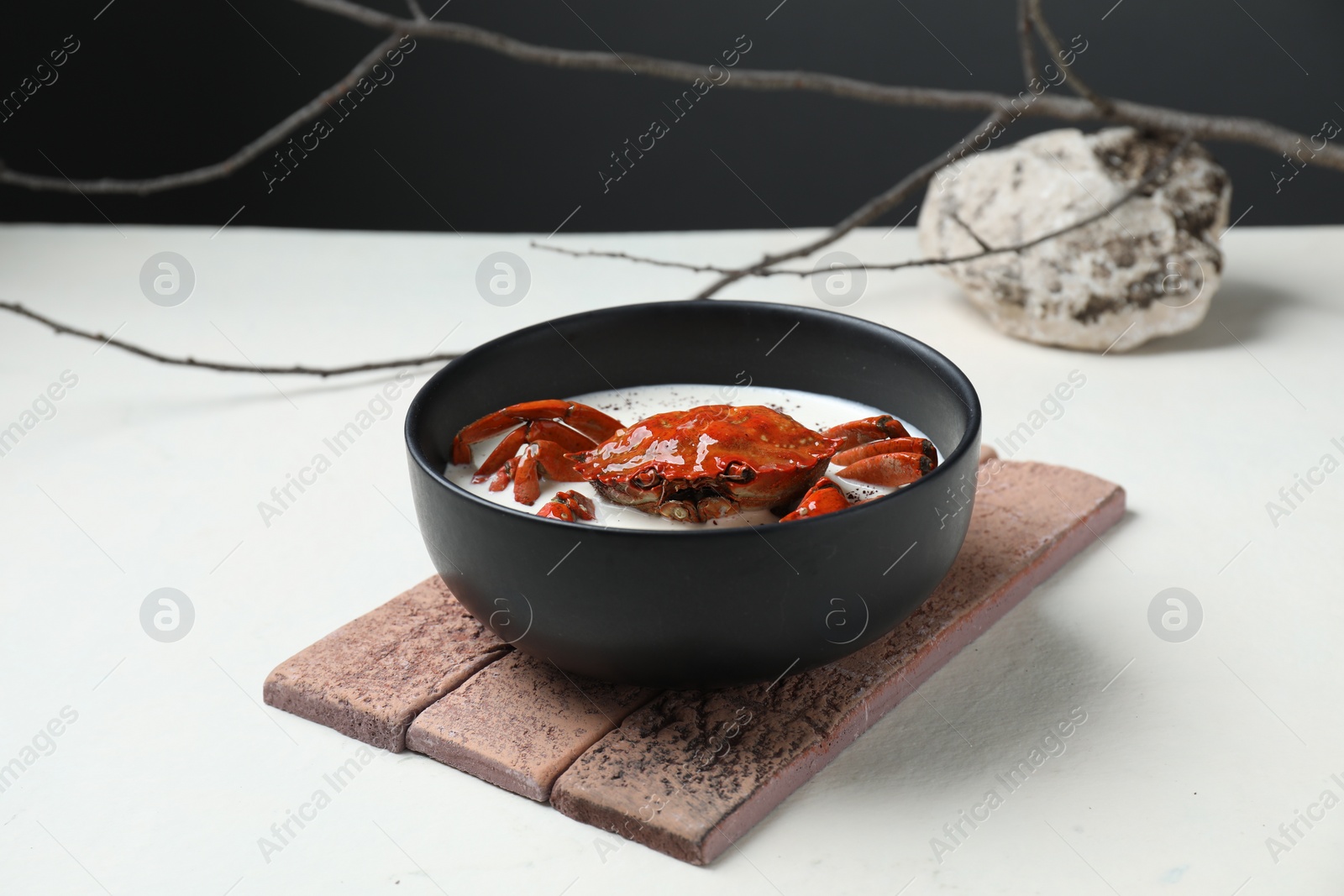 Photo of Delicious boiled crab with cream sauce in bowl on white table. Creative dish presentation