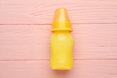 Photo of Feeding bottle with infant formula on pink wooden table, top view