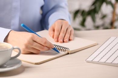 Photo of Woman writing in notebook at white wooden table indoors, closeup