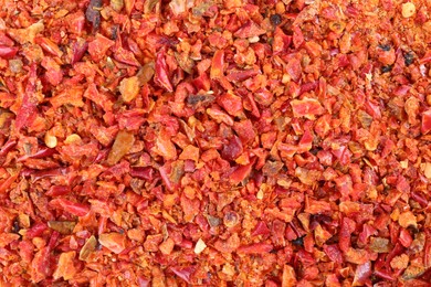 Photo of Aromatic spice. Red chili pepper flakes as background, top view