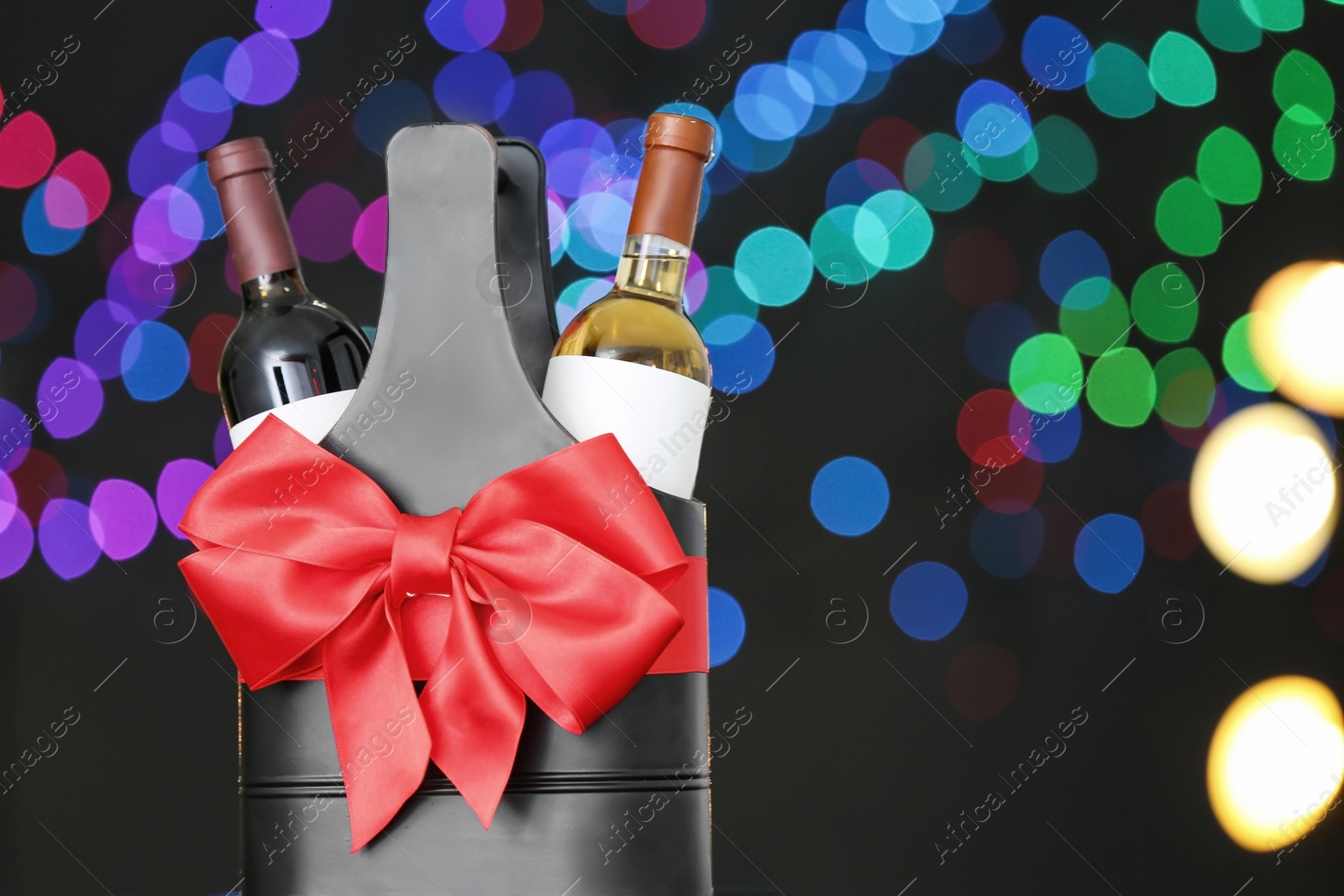 Photo of Festive package with bottles of wine against blurred lights, space for text. Bokeh effect