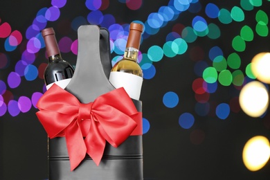 Festive package with bottles of wine against blurred lights, space for text. Bokeh effect