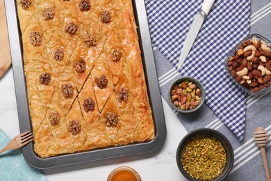 Delicious baklava with walnuts in baking pan and nuts on white table, flat lay