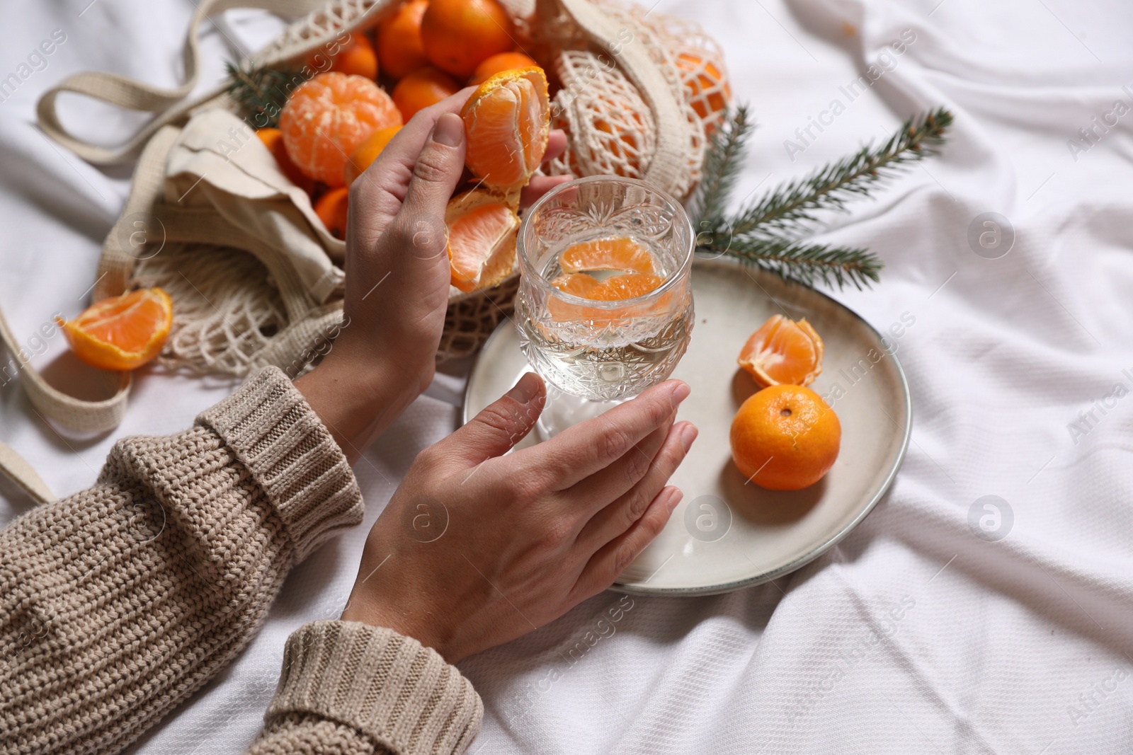 Photo of Woman with delicious ripe tangerines and glass of sparkling wine on white bedsheet, closeup