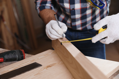 Photo of Professional carpenter measuring wooden plank at workbench, closeup