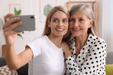 Photo of Happy daughter taking selfie with her mature mother at home