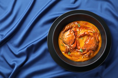 Delicious boiled crabs with sauce in bowl on blue tablecloth, top view. Space for text