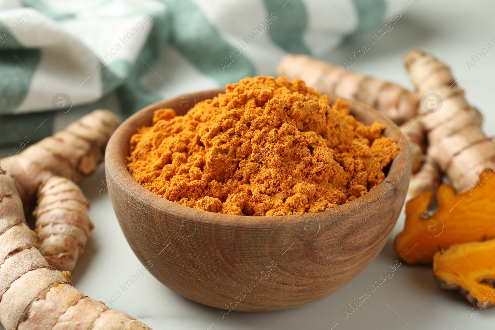 Photo of Aromatic turmeric powder and raw roots on white table, closeup