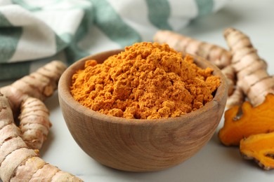 Photo of Aromatic turmeric powder and raw roots on white table, closeup