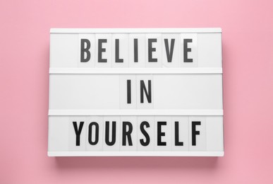 Photo of Lightbox with motivational quote Believe in Yourself on pink background, top view