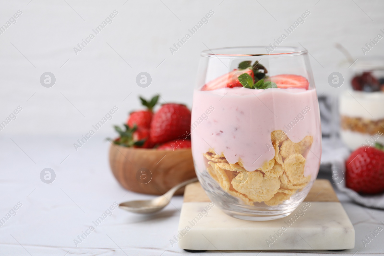 Photo of Glass with yogurt, strawberries and corn flakes on white textured table. Space for text