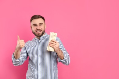 Young man with delicious shawarma on pink background, space for text